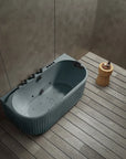 A top view of the Bellastone Doria spa bathtub in blue grey with black tap ware, in a modern bathroom with wooden floor and gray walls.