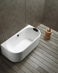 A top view of the Bellastone Doria back-to-wall bathtub in white, in a modern bathroom with wooden floor and gray walls.